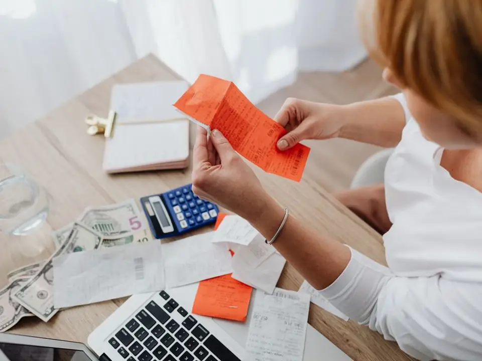 Mujer revisa recibos con una calculadora y una laptop